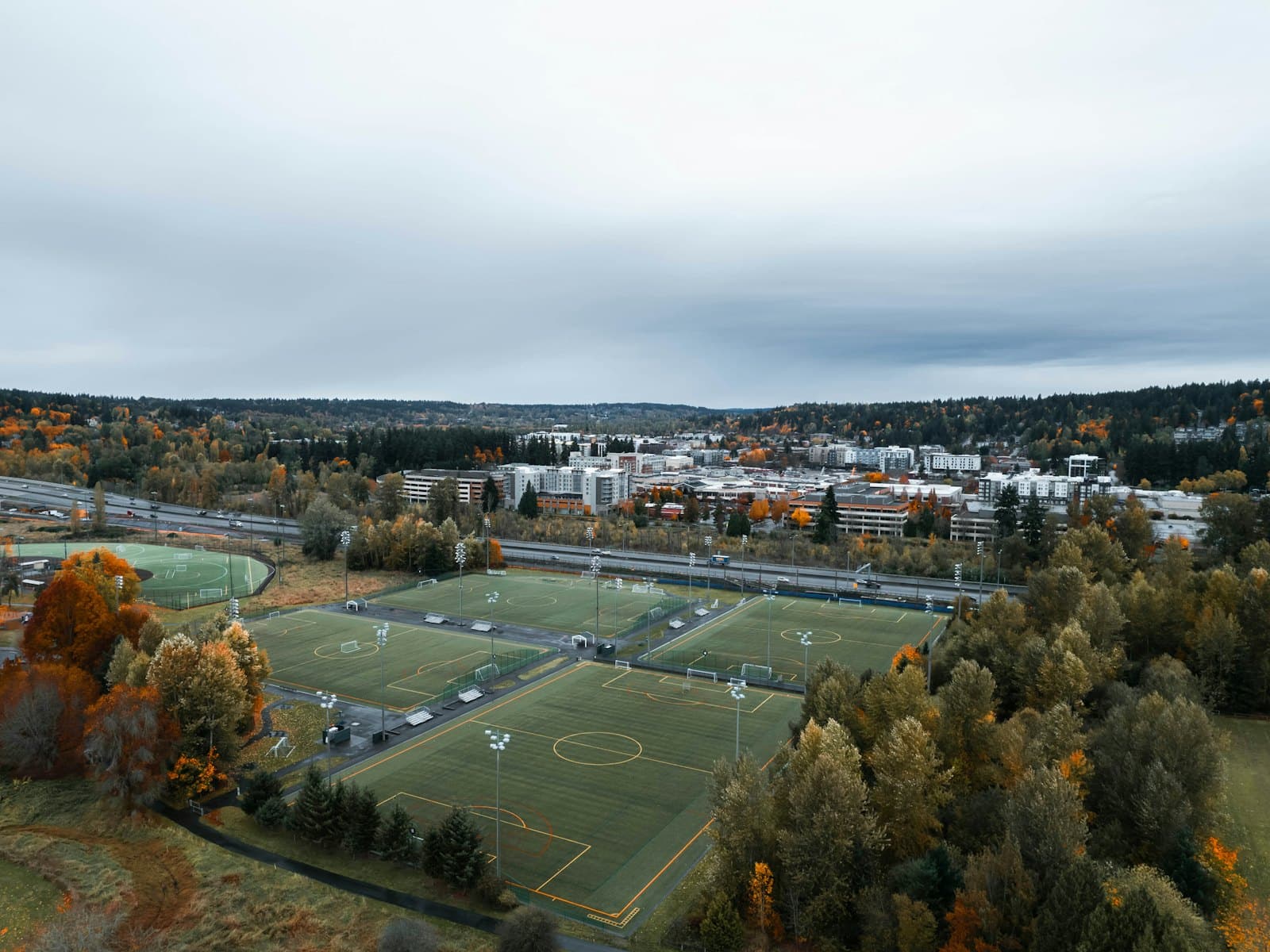 An aerial view of sports fields surrounded by autumn trees and low buildings