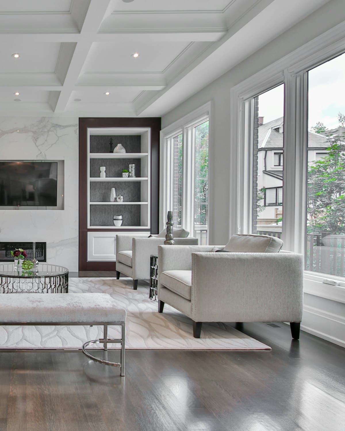 A bright staged living room with white armchairs and tall windows